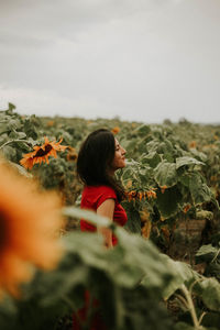 Woman standing amidst sunflower plants against sky