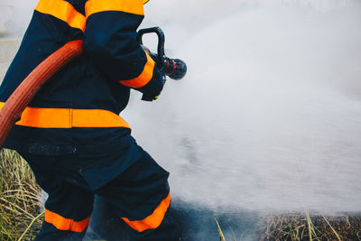 Rear view of firefighter spraying water on field