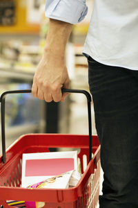 Cropped image of man carrying shopping basket in supermarket