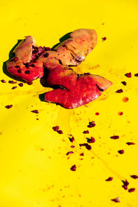 Crushed ripe red pomegranate with peel placed on bright yellow background with seeds and stains in light modern studio