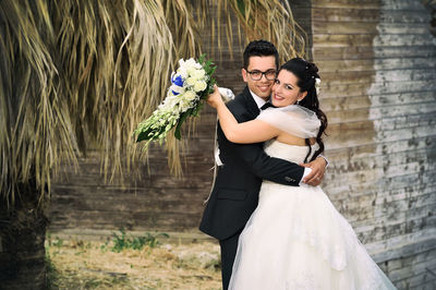 Portrait of happy young couple embracing while standing against wall