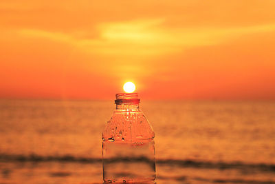 Electric lamp by sea against sky during sunset