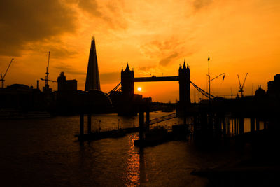 Silhouette of suspension bridge over river during sunset