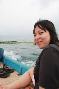 Portrait of smiling woman sitting in boat on sea against sky