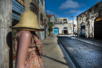Mannequin wearing hat on sidewalk amidst buildings