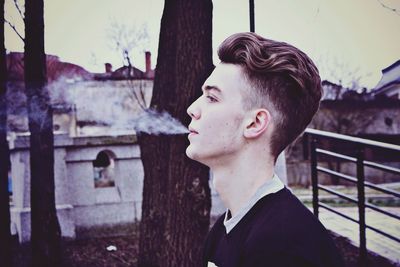 Close-up of young man exhaling smoke against sky