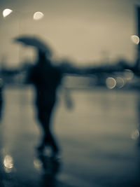 Defocused image of people standing by water against sky