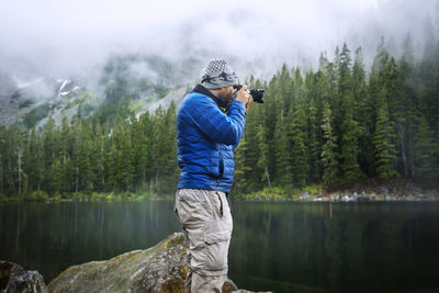 Side view of man photographing while standing against lake