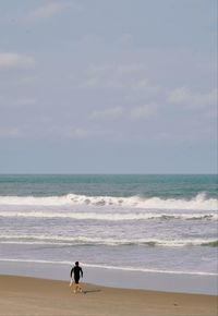 Rear view of woman walking at beach against sky