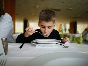 Cute boy having soup on table at restaurant