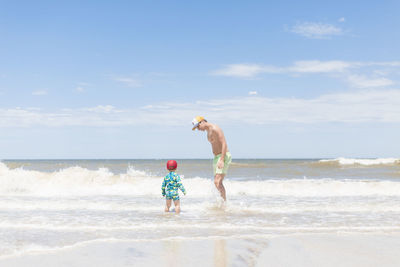 Full length of men and boy standing at beach against sky