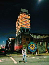 Full length of woman standing on illuminated street against buildings at night
