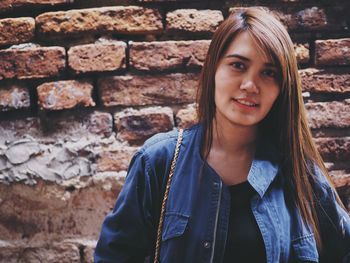 Portrait of smiling young woman against brick wall