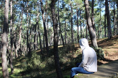 Side view of man wearing hooded shirt while sitting at forest