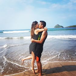 Couple kissing at beach against sky