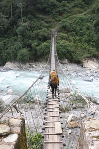 Man walking on rustic narrow footbridge over river