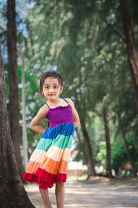 Pretty little girl wearing colourful dress and standing near the beach trees.