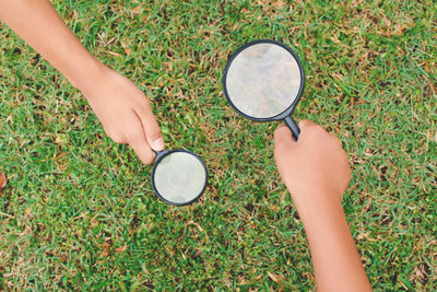 Cropped image of hands holding magnifying glasses on grassy field