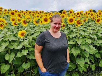 Portrait of smiling woman standing against sunflowers at field