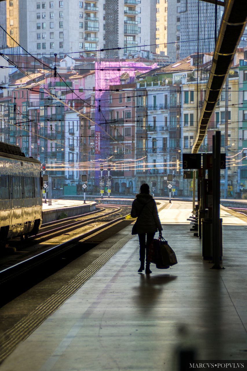 architecture, one person, building exterior, built structure, walking, city, full length, transportation, real people, mode of transportation, rear view, motion, rail transportation, travel, city life, building, adult, public transportation, lifestyles, outdoors, track, waiting