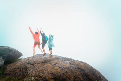 Rear view of women standing on rock against sky