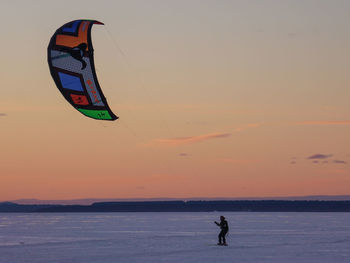 Man kiteboarding on snowcapped field at sunset