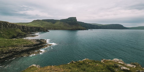 Scenic view of sea by mountain against sky