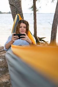 Brunette woman holds her mobile phone while relaxing on a hammock.