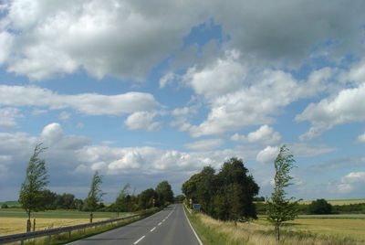 Road passing through landscape against storm clouds