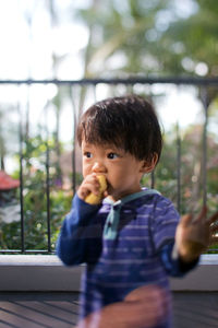 Cute boy eating food while looking away on balcony