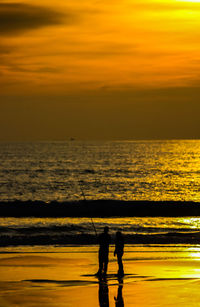 Silhouette people on beach against sky during sunset