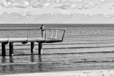 Rear view of man standing on pier over sea at beach