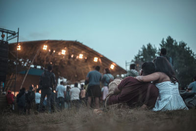 Rear view of couple sitting on grassy field against clear sky
