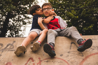 Portrait of smiling siblings sitting on concrete wall