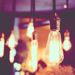 Close-up of illuminated light bulbs hanging at night