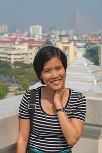 Portrait of woman smiling while standing on terrace in city