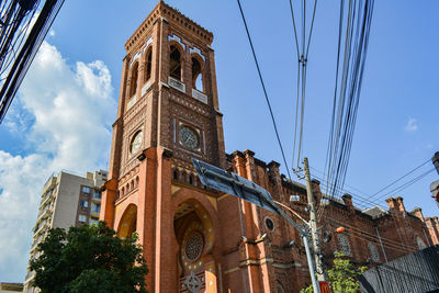 Low angle view of cross amidst buildings against sky