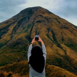Rear view of woman photographing on mobile phone against mountain
