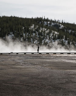 Man standing on boardwalk by geyser at yellowstone