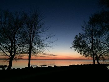 Silhouette bare trees by lake against sky at sunset