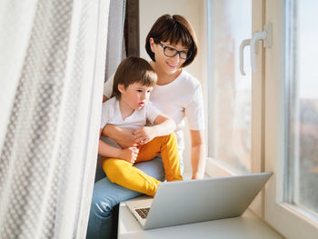 Woman remote works from home with laptop and son on knees. quarantine coronavirus covid19. 