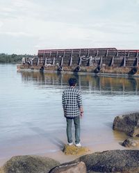 Rear view of man standing by lake against sky