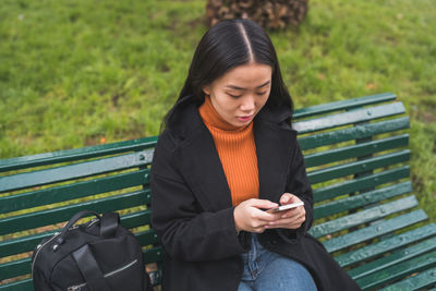 Woman using mobile phone while sitting on bench