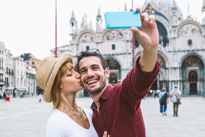 Woman kissing boyfriend taking selfie in city