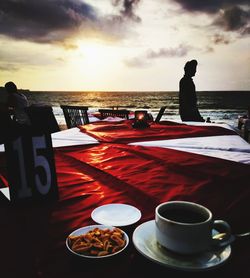 Coffee cup on table by sea against sky during sunset