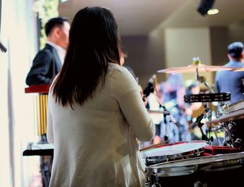 Rear view of female drummer playing drum during concert