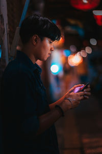 Side view of young man using mobile phone at night