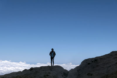 Man standing on rock against clear blue sky