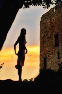 Silhouette woman standing by building against sky during sunset