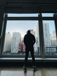 Rear view of man standing by window in city